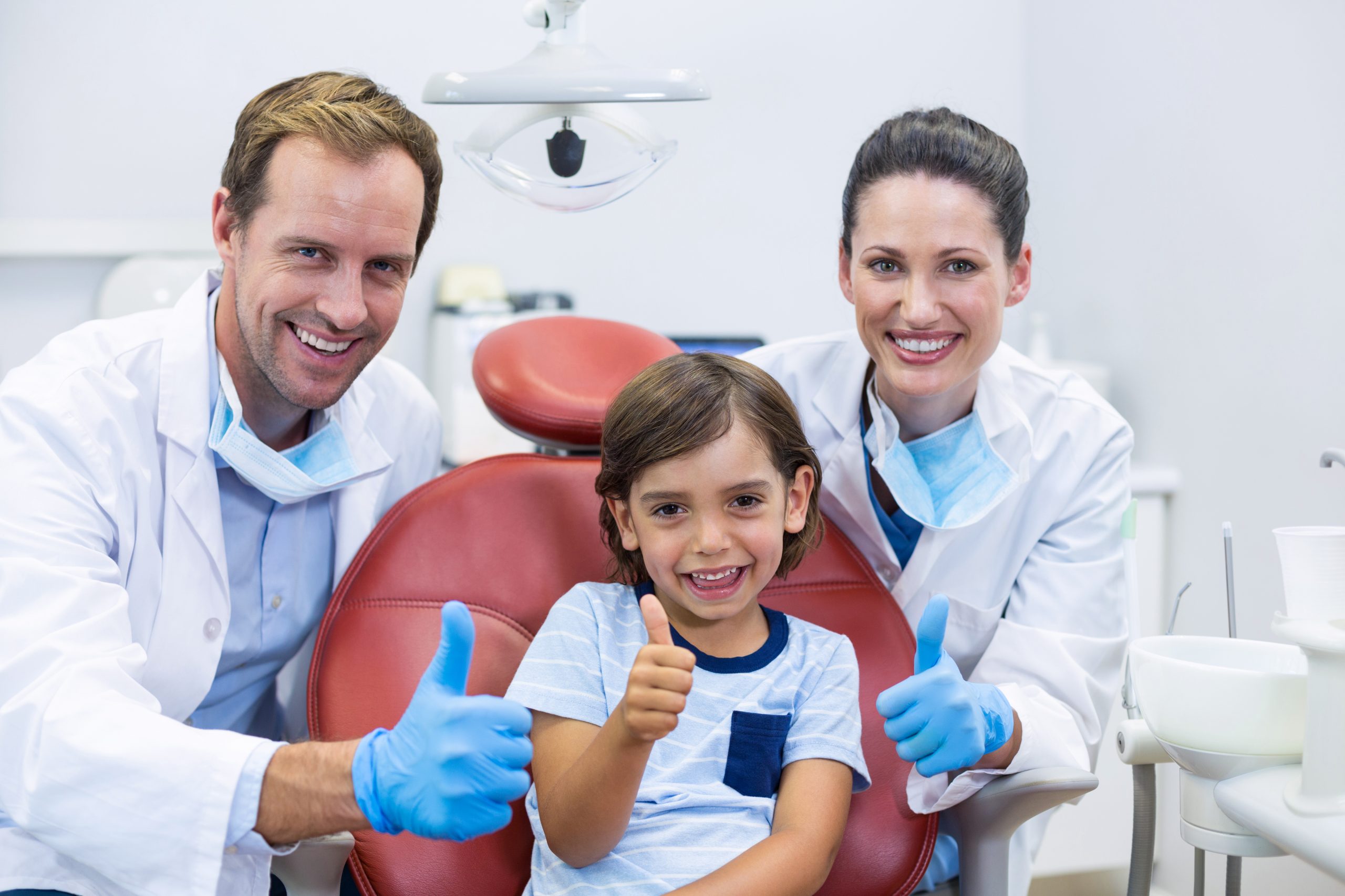Smiling dentists and young patient giving thumbs up in a modern dental clinic